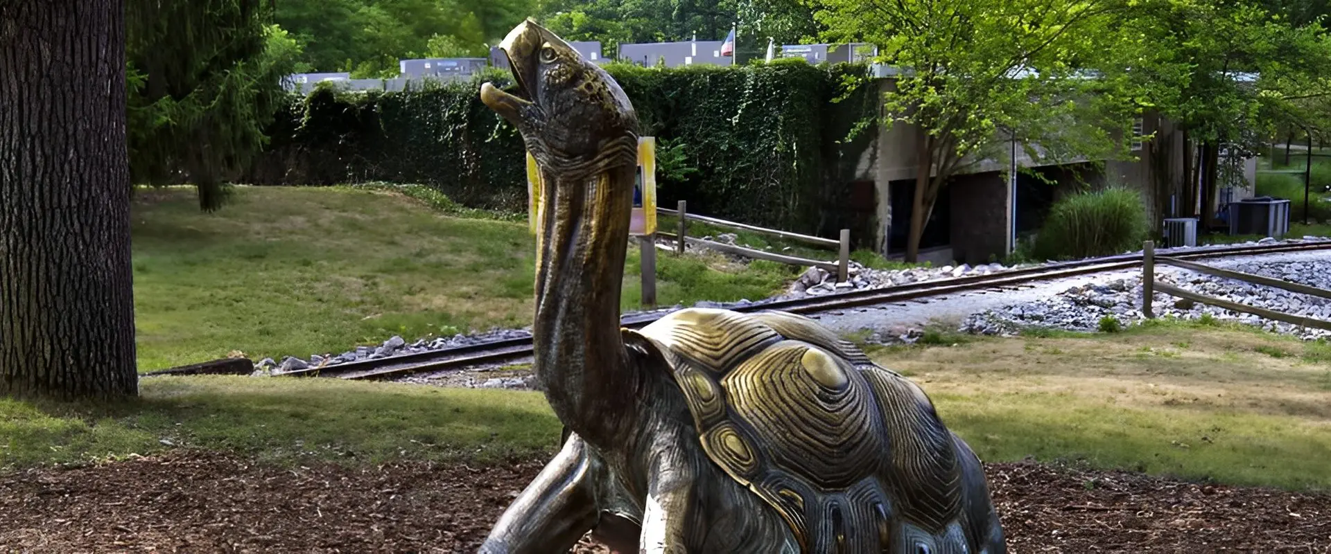 Turtle sculpture near railway tracks in park.